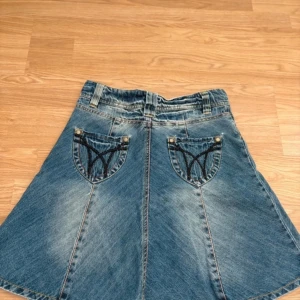 Utställd denimkjol - En denimkjol med utställd nederkant. Broderade fickor. Normal i storleken