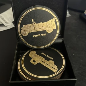 Volvo samlarkort i svart och guld - Säljer en samling runda samlarkort i svart med guldfärgade motiv av klassiska Volvo-bilar, bland annat Volvo 1927 och Volvo 1932. Kort i hård papp eller tunn plast, levereras i en svart ask. Perfekt för bilentusiaster och samlare.