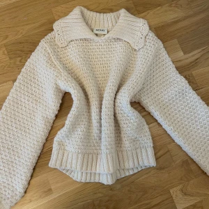 Vit stickad tröja med krage från Monki - Säljer en mysig vit stickad tröja från Monki med bred krage och strukturstickat mönster. Tröjan har långa ärmar och ribbade muddar vid ärmslut och nederkant. Perfekt för kyliga dagar!