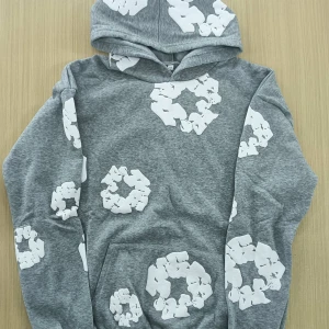 Grå hoodie med vita mönster - Säljer en grå hoodie med unika vita mönster över hela tröjan. Tröjan har huva och en stor ficka framtill. Perfekt för dig som vill ha en chill och snygg stil.