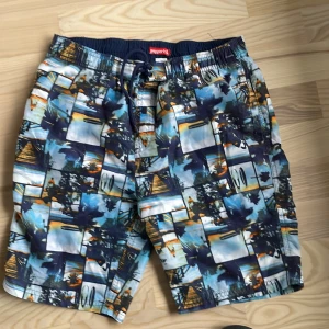 Mönstrade badshorts med palmmotiv - Säljer ett par färgglada badshorts från Supreme med tropiskt palmmotiv och elastisk midja med snörning. Shortsen har en lös passform och är perfekta för sommardagar vid stranden eller poolen.