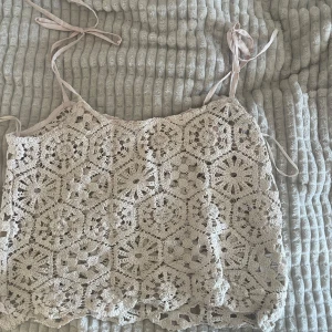 Beige virkad linnetopp - Superfin beige virkad linnetopp med smala axelband som knyts. Toppen har ett vackert blommigt mönster och är perfekt för sommardagar. Lätt och luftig, passar till både jeans och kjol.