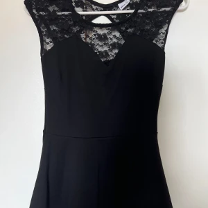 Svart topp med spets från Gina Tricot - Supersnygg svart topp från Gina Tricot med spets upptill och vid axlarna. Klänningen har en rund halsringning med transparent spetsdetalj och en klassisk, feminin siluett. Perfekt för dig som vill ha en elegant look.