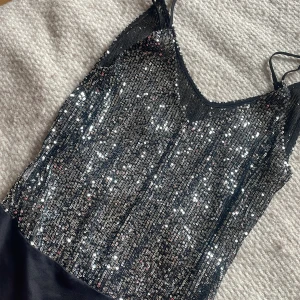 Svart glittrig bodysuit med paljetter  - Supersnygg Ibiza inspirerad svart bodysuit med tunna axelband och massor av glittrande paljetter framtill. Överdelen är täckt av silverfärgade paljetter som verkligen fångar ljuset, medan nedre delen är i slät svart tyg.