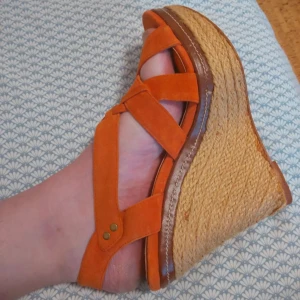 Orange sandaler med platåsula - Snygga sandaler i orange mocka med korsade remmar och öppen tå. Skorna har en hög platåsula i flätad jute som ger en somrig känsla. Perfekta för dig som vill sticka ut med färg och höjd på sommaren.
