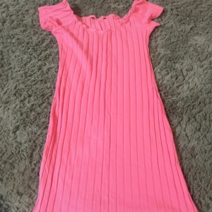 Klänning - Superfin rosa kortklänning med ribbad struktur och offshoulder-modell. Klänningen har korta ärmar och en söt, rynkad kant upptill. Perfekt för dig som vill sticka ut med en färgglad och trendig look.
