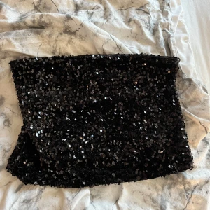 Svart paljett-tubtopp från H&M - Glittrig svart tubtopp från H&M, täckt med svarta paljetter som reflekterar ljuset snyggt. Modellen är bandeau och helt axelbandslös, perfekt för att sticka ut. Mjuk insida för extra komfort. Aldrig använd 