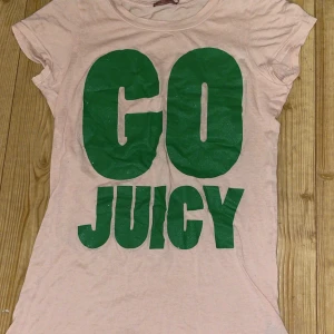 Juicy Couture rosa t-shirt med tryck - Ljusrosa t-shirt från Juicy Couture med stort grönt glittrigt tryck 'GO JUICY' på framsidan. Klassisk passform med korta ärmar och rund hals. Tillverkad i mjuk bomull, perfekt för en chill och trendig look.
