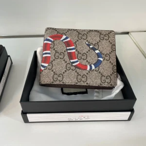 plånbok med ormmotiv  - Säljer en snygg plånbok med klassiskt GG-mönster i beige och brunt. Plånboken har en cool röd, blå och vit orm på framsidan som ger en unik touch. Perfekt accessoar för dig som vill sticka ut med stil.