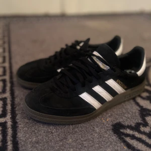 Adidas Spezial svartvita sneakers storlek 38 2/3 - Klassiska Adidas Spezial sneakers i svart mocka med vita läderdetaljer och de ikoniska tre ränderna på sidorna. Skorna har svart snörning, gummisula och rund tå. Perfekta för dig som gillar retrostil och streetwear.