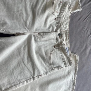 Vita raka boyfriend jeans från Bershka - Snygga vita jeans från Bershka i rak modell med klassiska fem fickor och diskreta röda detaljer vid sömmarna. Jeansen är tillverkade i bomull och har en oversized passform med midja och dragkedja framtill. Använt en gång!