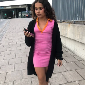 Rosa ribbad kortklänning med orange krage - Säljer en superfin rosa ribbad kortklänning med orange krage och v-ringning. Klänningen är tight och har kort ärm, perfekt för dig som vill sticka ut med färg. Snygg och bekväm att bära under varma dagar.