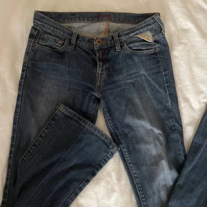 Replay lågmidjade utsvängda jeans  - Snygga blå jeans från Replay med klassisk femficksmodell och coolt broderi på bakfickorna. Jeansen har en rak passform och detaljer i gult på fickorna.   Midjemått: 38 cm tvärs över.  Innerbenslängd:80 cm.
