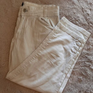 vita trekvartsbyxor med knappar i benslut - Snygga vita trekvartsbyxor i bomull coola tryckknappar vid bensluten. Perfekta för en clean och stilren look.