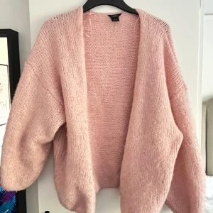 Ljusrosa stickad kofta från Lindex - Ljusrosa stickad kofta från Lindex. Koftan har en öppen front utan knappar, breda ärmar och en fluffig känsla som gör den perfekt att slänga på sig när det är kyligt. Slutsåld!!!