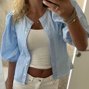 Ljusblå skjorta med puffärm - Säljer en ljusblå skjorta med puffiga trekvartsärmar och knappar framtill. 