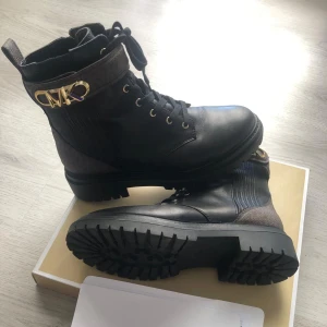 Svarta boots från Michael Kors - Snygga svarta boots från Michael Kors med guldfärgad MK-detalj vid ankeln. Skorna är som nya och knappt använda.