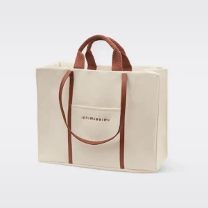 Beige strandväska från Intimissimi - Stilren strandväska i beige färg med bruna handtag och axelremmar. Väskan har en fyrkantig form, ytterficka med broderad logga och rymligt huvudfack. Perfekt för att bära allt du behöver ha med dig.