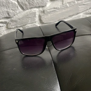 Svarta solglasögon med mörka glas - Stilrena svarta solglasögon med rektangulär form och mörka tonade glas. Klassisk design som passar till de flesta outfits och ger en cool vibe. Bågarna är i plast och glasen har en snygg övergång från mörkt till ljusare ton. Trendiga glajjor som passar alla 10/10 skick 