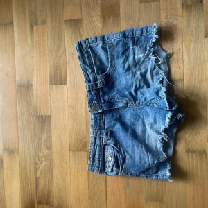 Blå jeansshorts från Gina Tricot - Snygga blå jeansshorts från Gina Tricot med fransig, rå kant både fram och bak. Fickor där bak med knappar. Shortsen är lågmidjade 