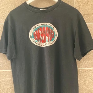 Svart Supreme t-shirt med tryck - Supreme t-shirt i svart med stort färgglatt Supreme-tryck på bröstet och lista med städer och telefonnummer på ryggen. Klassisk passform och tillverkad i 100% bomull. Perfekt för dig som gillar streetwear och vill sticka ut.