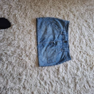 Blå jeanskjol med stora fickor - Snygg blå jeanskjol i kort modell med stora fram- och bakfickor. Klassisk denimlook med bälteshällor och knapp framtill. Perfekt för dig som gillar en avslappnad och trendig stil.