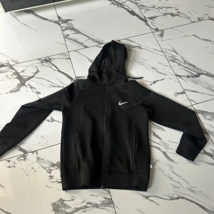 Svarta mjukisbyxor från Nike M - Svarta mjukisbyxor från Nike i storlek M. Byxorna har resår och snörning i midjan, två fickor med dragkedja och Nike-logga på låret. Tillverkade i mjukt material som passar perfekt för chill eller träning.