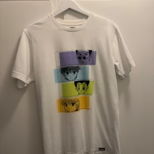 Vit t-shirt med tryck från Uniqlo - Vit t-shirt från Uniqlo med färgglatt tryck framtill som visar fyra Hunter x Hunter karaktärer i lila, blå, grön och gul ruta. Klassisk passform med rund hals och korta ärmar. Den är i mycket bra skick och tillverkad i 100% bomull. Postas ca 1-3 dagar efter köp. Frågor? Skicka ett dm!