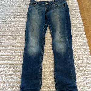 Blå slim jeans från Jack & Jones - Snygga blå jeans från Jack & Jones i slim fit-modell. Jeansen har klassisk femficksdesign och ljusa partier framtill för en cool, använd look. Tillverkade i mjukt denimtyg med orangea sömmar och normal midja. Jeansen har ett litet ihopsytt hål på knät som inte syns.