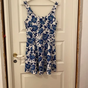 Blommig kortklänning från H&M Divided - Superfin vit kortklänning från H&M Divided med blått blommönster. Klänningen är ärmlös med rundad urringning och har en lätt utställd kjol. Perfekt för sommarens alla tillfällen och riktigt skön att bära. Pris kan diskuteras!