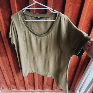 Olivgrön topp från Ellos - Säljer en olivgrön topp från Ellos i storlek 44. Den har en avslappnad passform med korta ärmar och en rund halsringning. Perfekt för en casual look!