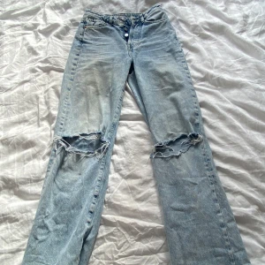 Blå slitna jeans - Säljer ett par blå jeans med hål vid knäna. De har en straight passform och är i en ljusblå tvätt. säljer pågrund av att dem e föör små!