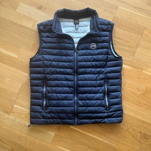 Mörkblå quiltad dunväst från Club - Säljer en snygg mörkblå quiltad dunväst från Colmar. Västen har en dragkedja framtill och två praktiska fickor med dragkedjor. Perfekt för lager-på-lager under höst och vår. Den är i bra skick och superbekväm att ha på sig!