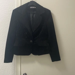 Svart kavaj från Nouran Mod - Säljer en elegant svart kavaj från Nouran Mod. Den har en klassisk design med en knapp framtill och är tillverkad i ett mjukt material som ger en lyxig känsla. Perfekt för både formella och semi-formella tillfällen.