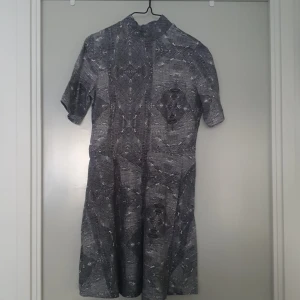 Mönstrad klänning i grå toner - Säljer en unik klänning med ett coolt geometriskt mönster i grå och svarta toner. Klänningen har korta ärmar och en bekväm passform som passar perfekt för både vardag och fest. Materialet känns mjukt och skönt mot huden.