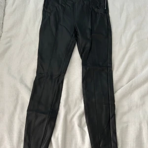 Svarta leggings från Amisu - Säljer ett par svarta leggings från Amisu i storlek 38. De är gjorda i ett syntetmaterial som ger en skinnliknande look. 