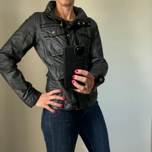 Svart jacka med dragkedja - Säljer en snygg svart jacka med dragkedja och knappar. Den har en cool stil med flera fickor och en hög krage. Perfekt för höst och vår, och den är i bra skick. Passar till både vardag och fest!