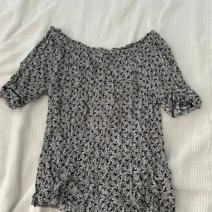 Svartvit blommig topp från C - Säljer en superfin svartvit blommig topp från Cubus. Den har en offshoulder-design och korta ärmar.