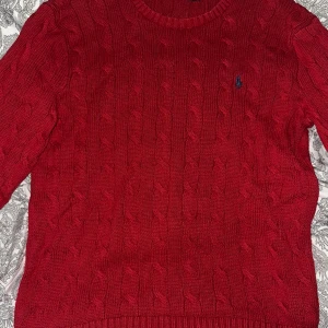 Röd stickad tröja från Ralph Lauren - Snygg röd stickad tröja från Ralph Lauren med kabelstickat mönster. Tröjan har långa ärmar och en rund halsringning. Perfekt för en skön mer upprättad look. Pris kan diskuteras och frågor besvaras så snabbt som möjligt.