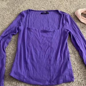 Lila ribbad topp från BikBok - Säljer en snygg lila ribbad topp från BikBok. Toppen har en fyrkantig halsringning och långa ärmar, perfekt för både vardag och speciella tillfällen. Den är i storlek S och har en skön passform.
