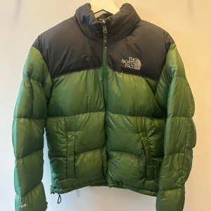 Grön och svart dunjacka från The North Face - Säljer en grön och svart dunjacka från The North Face. Jackan har en dragkedja framtill och är långärmad. Perfekt för kyliga dagar med sin pufferdesign som håller värmen.