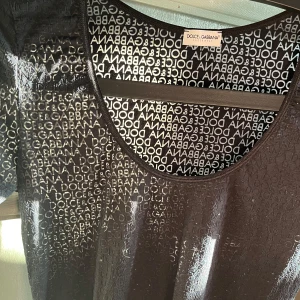Svart top från Dolce & Gabbana - Snygg svart uringad top från Dolce & Gabbana med korta ärmar och ett transparent mönster av märkesloggan över hela tyget. Perfekt för en stilren look.