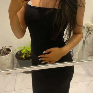 Svart axelbandslös klänning - Elegant svart axelbandslös klänning med smala axelband. Perfekt för en stilren look. Klänningen är figurnära och har en klassisk design.