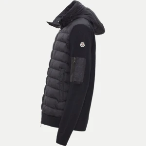 Svart pufferjacka från Moncler - Snygg svart pufferjacka från Moncler med långärmad design och dragkedja. Jackan har en quiltad stil och en praktisk ficka på armen. Det ända felet är vid luvan en av sträckorna sönder men syns knappt. Äkta! Storlek m