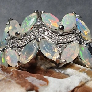 Silver ring med opaler och kristaller - En fantastisk ring prydd med skimrande opaler och gnistrande kristaller. Ringen har en elegant design med flera ovala opaler i en vågformad uppsättning, infattade i silver. Perfekt för att ge en touch av glamour till vilken outfit som helst.     Produkt beskrivning: 925 silver, stenar: 12 st Etiopiska opaler fasetterad, ca 6x3 mm - 1.848ct, 20 st runda zirkoner ca 1 mm - 0,400ct och 5 st runda zirkoner ca 1,5 mm - 0,100ct Ring storlek: 18.3 mm  ( Q )