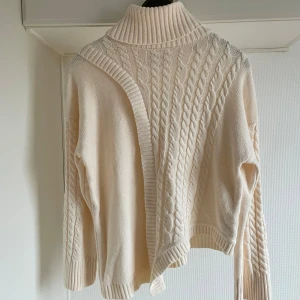 Beige stickad polotröja M - Säljer en mysig beige stickad polotröja med kabelstickat mönster. Tröjan har långa ärmar och en hög krage som håller dig varm under kyliga dagar. Perfekt för höst och vinter!