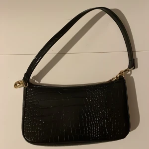 Svart axelväska med krokodilmönster - Snygg svart axelväska med krokodilmönster och guldfärgade detaljer. Väskan har en dragkedja, och en ficka i insidan. 
