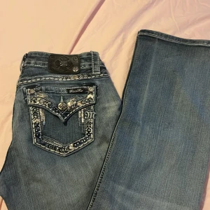 MISS ME jeans - Snygga blå jeans från Miss Me med unika broderade detaljer och paljetter på bakfickorna. Jeansen har en lågmidjad passform och är bootcut. Kan tänka mig sänka priset. Hör av er vid frågor om byxorna osv. Finns fläck men går bort i tvätt