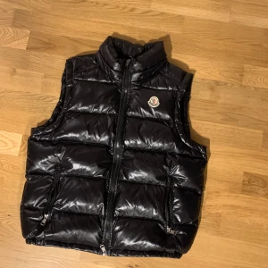 Moncler väst - Säljer min feta moncler väst med glansig finish och dragkedja framtill. Västen har en avtagbar huva och två praktiska fickor med dragkedjor. Den är helt ny och har endast används en gång.