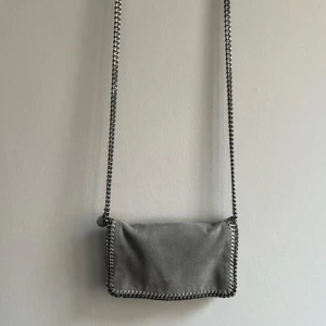 Grå axelväska med kedjedetaljer - Snygg grå axelväska med kedjedetaljer runt kanterna och en lång kedjerem. Perfekt för att ge en stilren touch till din outfit.